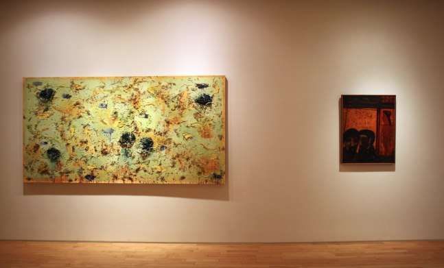 Photograph showing a view of an exhibition, with two framed paintings hanging on a white wall