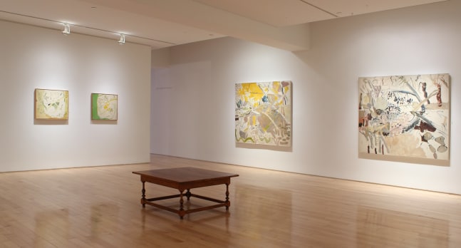 Photograph showing a corner view of an exhibition space, with four paintings hanging on white walls