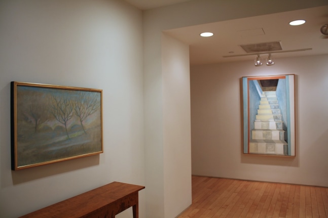 Photograph showing a view of an exhibition space, with two framed paintings hanging on white walls