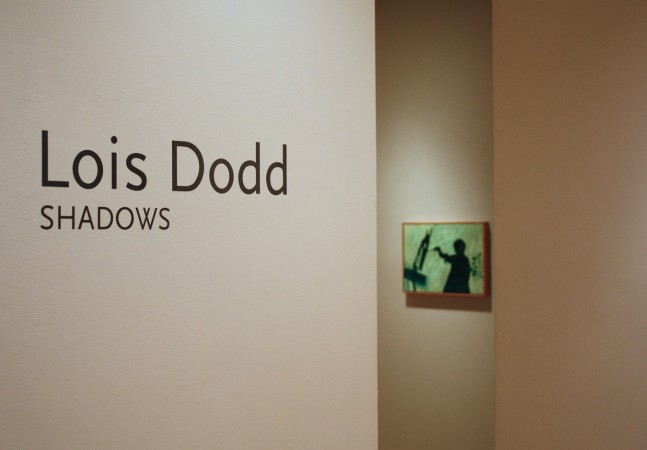 Photograph showing a view of an exhibition space, with wall text that reads &quot;Lois Dodd: Shadows&quot; on the wall to the left, and a small painting hanging on a wall in the background