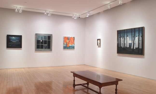Photograph showing a corner view of an exhibition space, with five paintings hanging on white walls