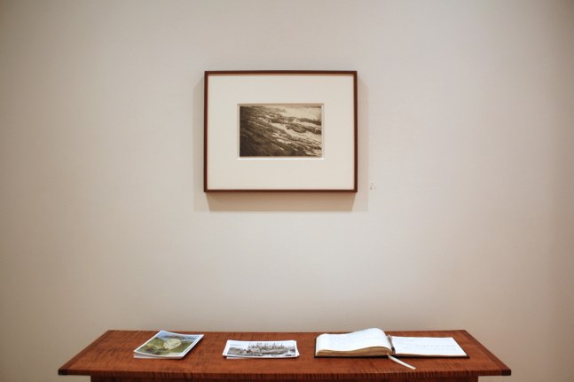 Photograph showing a view of an exhibition, with one small framed drawing hanging over a wooden table
