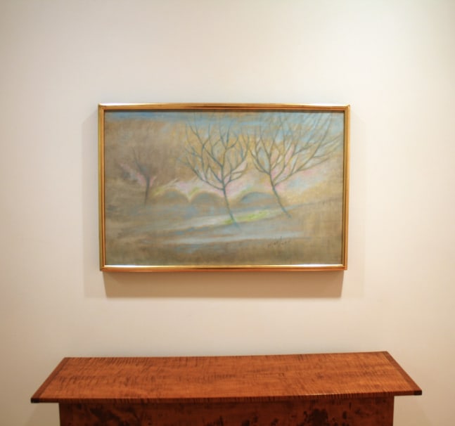 Photograph showing a view of an exhibition, with one framed painting hanging over a wooden table