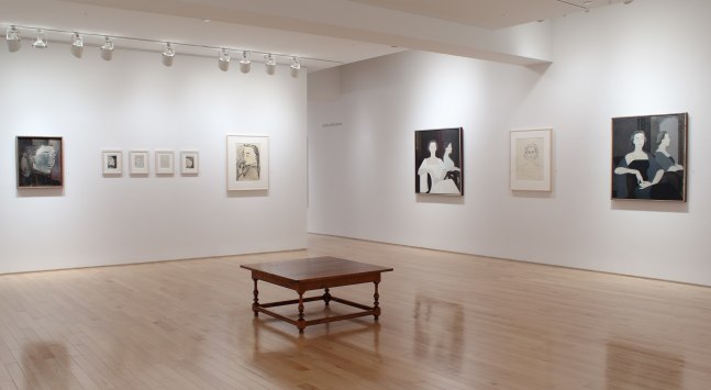 Photograph showing a corner view of an exhibition space, with nine paintings hung on white walls