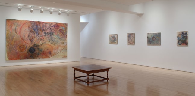 Photograph showing a corner view of an exhibition space, with five paintings hung on white walls