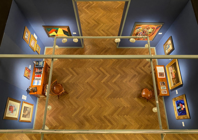 Photograph showing an aerial view of an exhibition booth, with eleven paintings hung on three blue walls