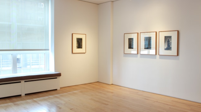 Photograph showing a corner view of an exhibition space, with four framed drawings hanging on white walls