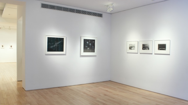 Photograph showing a corner view of an exhibition space, with five framed drawings hanging on white walls