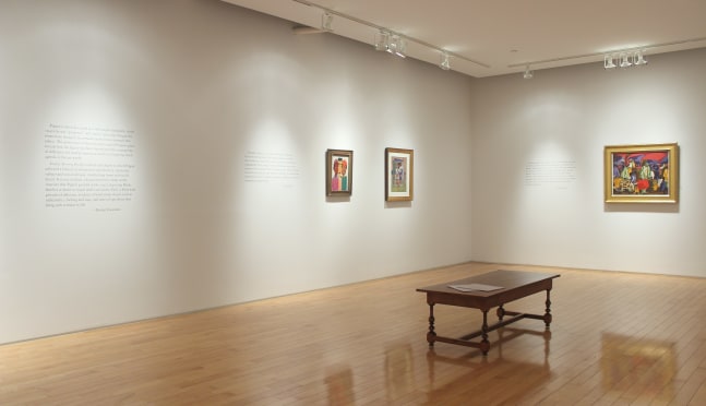 Photograph showing a corner view of an exhibition space, with three paintings hanging on white walls