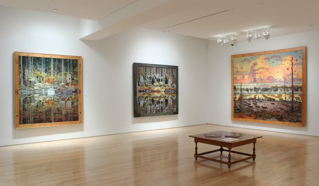 Photograph showing a corner view of an exhibition space, with three paintings hanging on white walls