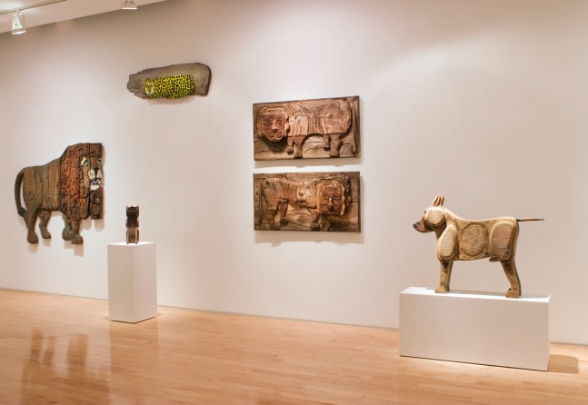 Photograph showing a view of an exhibition space, with four sculptures hanging on the walls and two sculptures on pedestals
