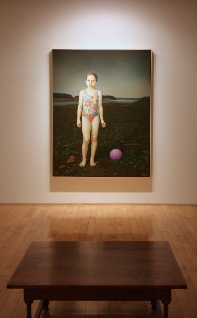 Photograph showing a view of an exhibition space, with one large framed painting hanging on a white wall