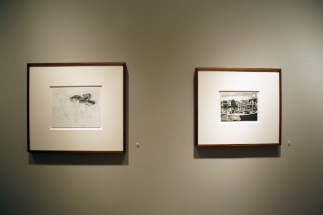 Photograph showing a view of an exhibition, with two small framed drawings hanging on a grey wall