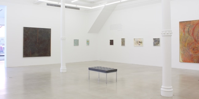 Photograph showing a corner view of an exhibition space, with eight paintings hanging on white walls