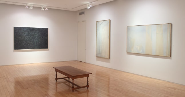 Photograph showing a corner view of an exhibition space, with three large paintings hanging on white walls