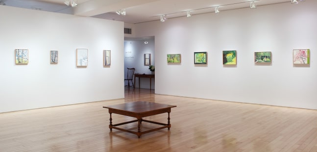 Photograph showing a corner view of an exhibition space, with nine small framed paintings hanging on white walls