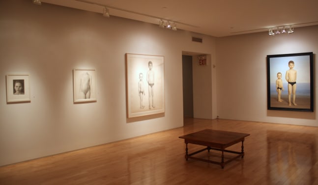 Photograph showing a corner view of an exhibition, with a large framed painting, a large framed drawing, and two small framed drawings hanging on white walls