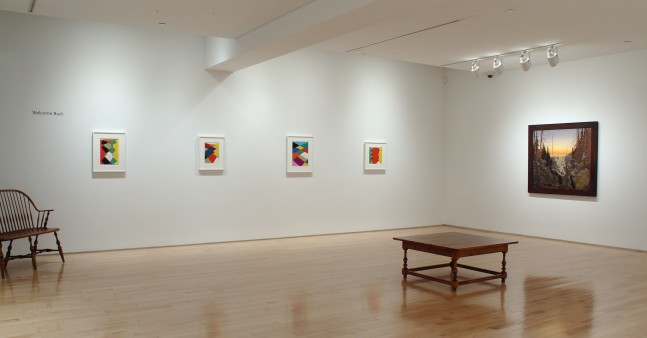 Photograph showing a corner view of an exhibition space, with five paintings hung on white walls