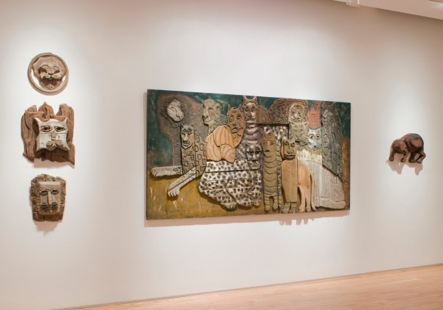 Photograph showing a view of an exhibition space, with one large sculptures and four smaller sculptures hanging on the wall