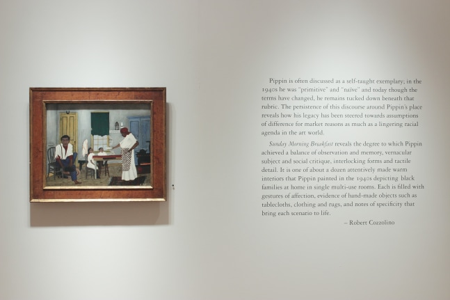 Photograph showing a view of an exhibition space, with one small painting hanging beside a block of wall text
