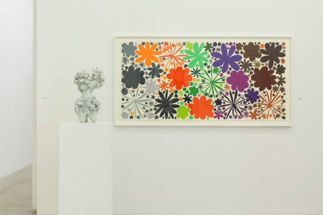 Photograph of a detail view of an exhibition with a framed print hanging on a white wall and a porcelain sculpture on a pedestal in front