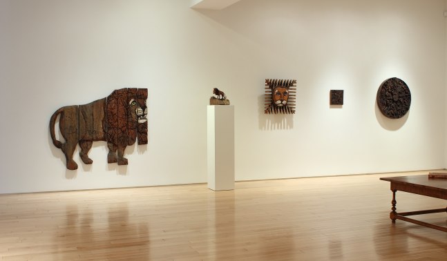Photograph showing a view of an exhibition space, with four sculptures hanging on the wall and one small sculpture on a pedestal