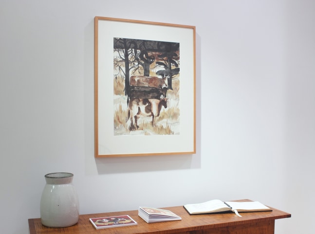 Photograph of an exhibition space showing a framed drawing hanging on a white wall over a wooden table