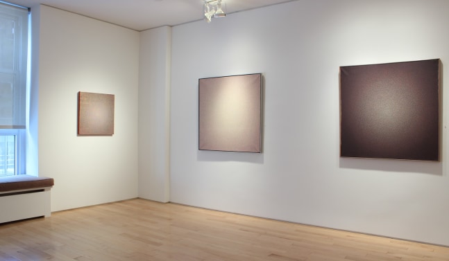 Photograph showing a corner view of an exhibition space, with three paintings hanging on the white walls