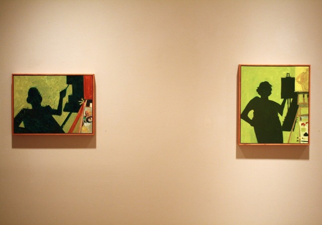 Photograph showing a view of an exhibition, with two small framed paintings hanging on a white wall