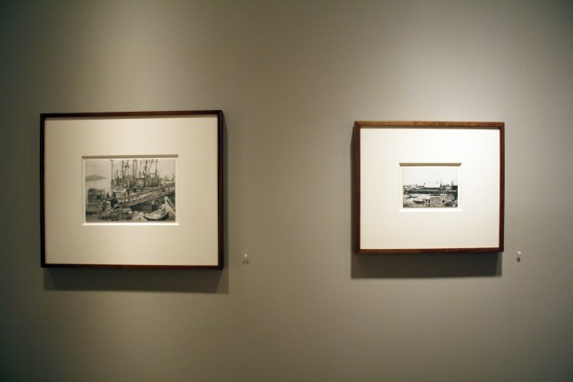 Photograph showing a view of an exhibition, with two small framed drawings hanging on a grey wall