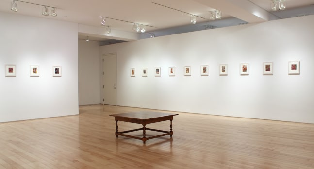 Photograph showing a corner view of an exhibition space, with thirteen small framed paintings hanging on white walls