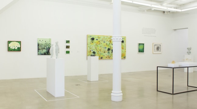 Photograph of a view of an exhibition, showing eight paintings of varying sizes hanging on the wall and six sculptures on pedestals throughout a white exhibition space