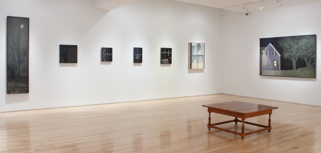 Photograph showing a view of an exhibition space with seven paintings hanging on a white wall