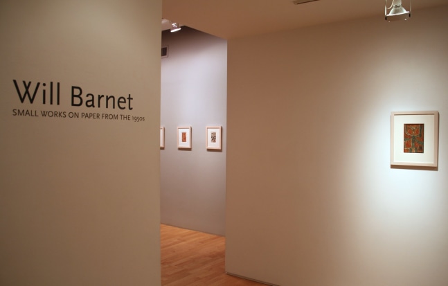 Photograph showing a view of an exhibition space, with four small framed paintings hanging on the walls and wall text that reads &quot;Will Barnet: Small Works on Paper from the 1950s&quot; on the wall to the left
