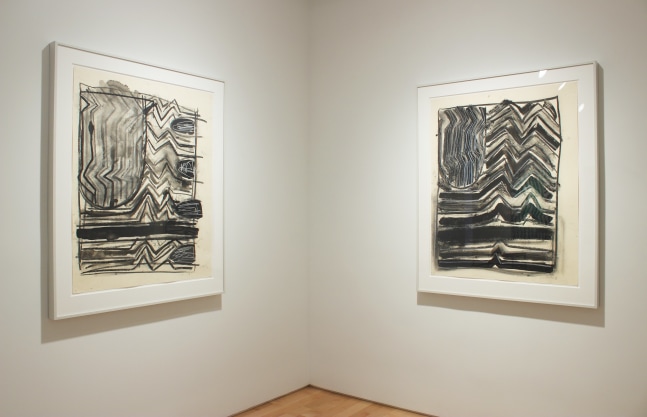 Photograph showing a corner view of an exhibition space, with two framed drawings hanging on white walls