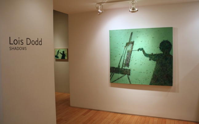 Photograph showing a view of an exhibition space, with two paintings hanging on the walls, and wall text that reads &quot;Lois Dodd: Shadows&quot; on the wall to the left