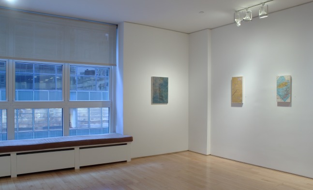 Photograph showing a corner view of an exhibition space, with three paintings hung on white walls