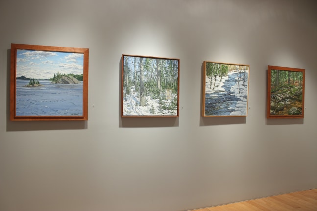 Photograph showing a view of an exhibition space, with four framed paintings hanging on a wall