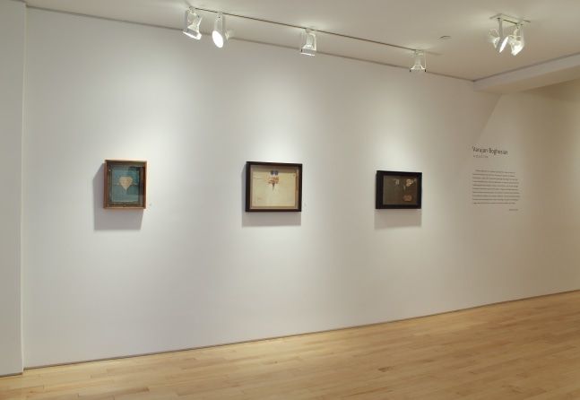 Photograph showing a view of an exhibition space with three paintings hanging on a white wall