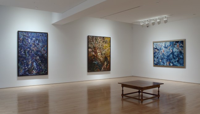 Photograph showing a corner view of an exhibition space with three paintings hanging on white walls