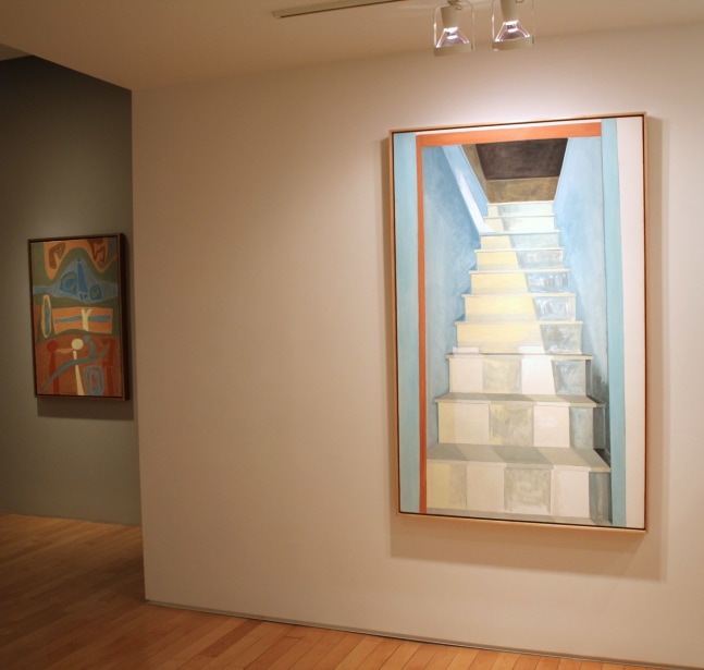 Photograph showing a view of an exhibition, with two framed paintings hanging on the walls