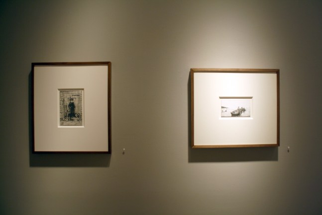 Photograph showing a view of an exhibition, with two small framed drawings hanging on a grey wall