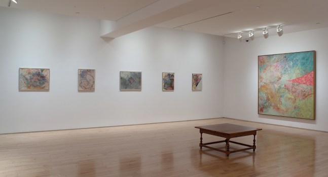 Photograph showing a corner view of an exhibition space, with six paintings hanging on white walls