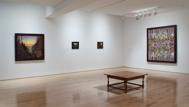 Photograph of a corner view of an exhibition space, with four paintings hung on white walls