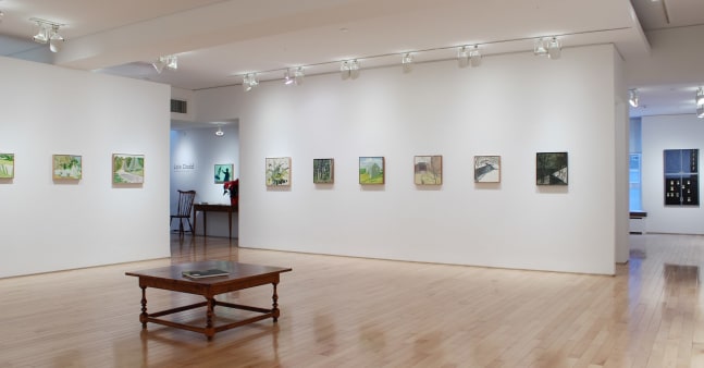 Photograph showing a corner view of an exhibition space with nine paintings hanging on white walls