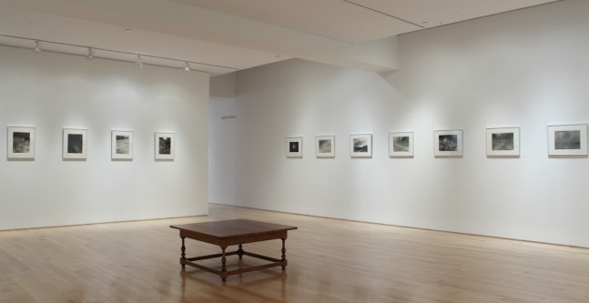 Photograph showing a corner view of an exhibition space, with eleven framed drawings hanging on white walls