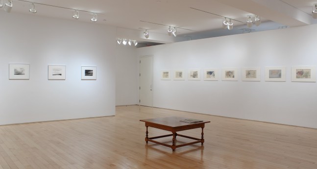 Photograph showing a corner view of an exhibition space, with eleven drawings hanging on white walls.