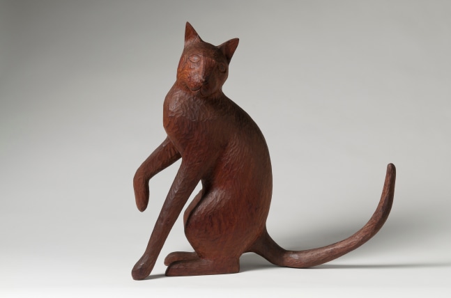 Wood sculpture of a cat sitting on its hind legs, with one forepaw slightly raised