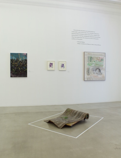 Photograph of a detail view of an exhibition with four paintings hung on a white wall with a sculpture on the ground in front