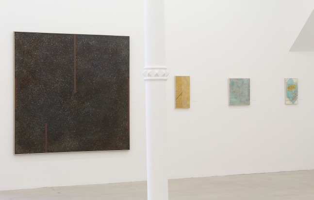 Photograph showing a view of an exhibition space, with four paintings hanging on a white wall